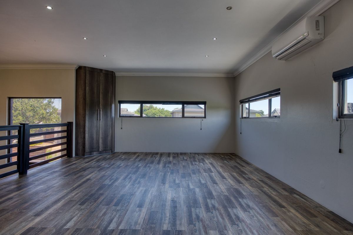 Spacious bedroom featuring timber-look laminate flooring, recessed lighting, a built-in corner cupboard, and a wall-mounted air conditioning unit.