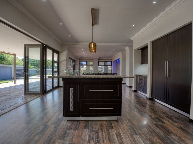 Modern kitchen featuring a central island with granite countertops, dark wood cabinetry, and seamless access to the outdoor patio through large stacking glass doors.