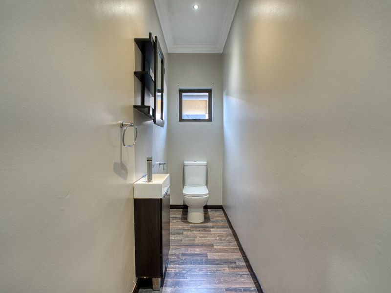 A compact guest bathroom featuring a modern vanity, basin, and toilet with wood-look laminate flooring and neutral wall finishes.