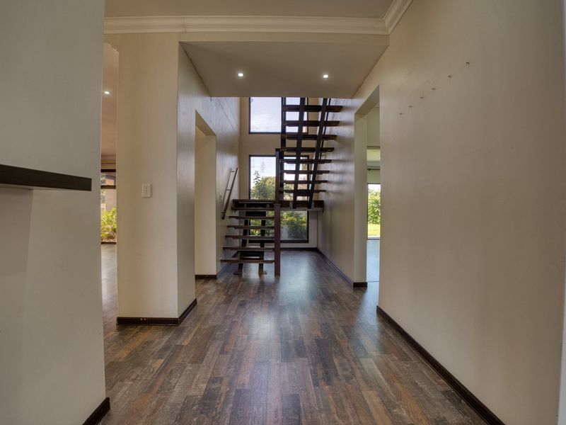 Spacious entrance hallway featuring modern open-tread staircase, recessed lighting, and durable laminate flooring, leading into an open-plan living area.