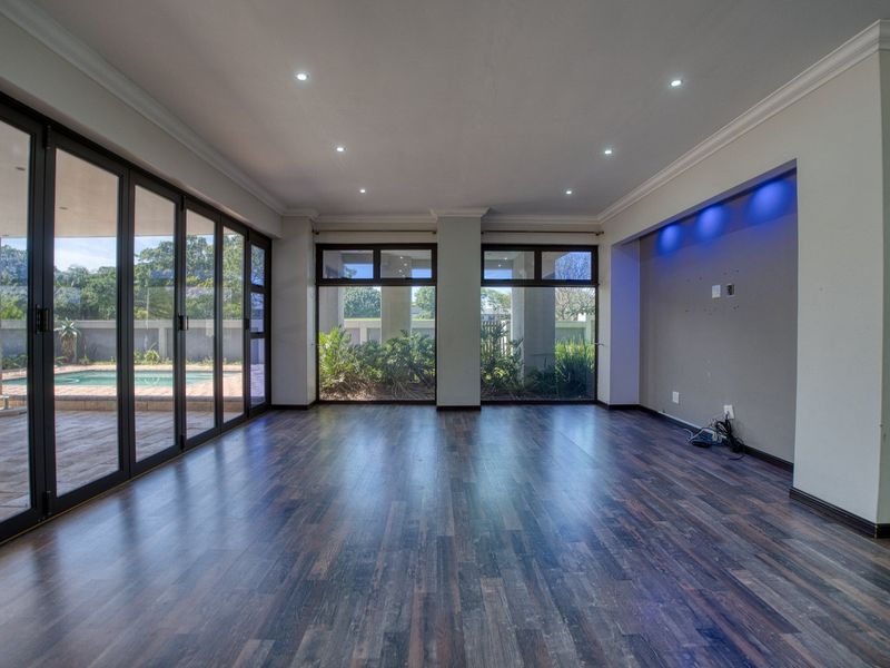 Spacious, empty living room featuring dark laminate flooring, recessed lighting, and large sliding glass doors opening to a patio and pool area.