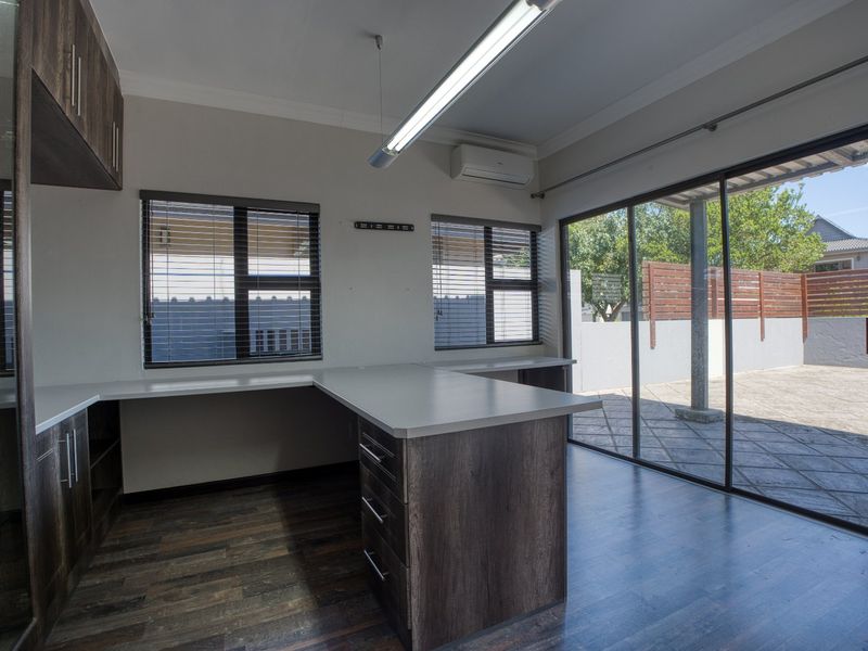 A bright, modern home office featuring built-in desk cabinetry, laminate flooring, and large sliding glass doors providing direct access to the outdoor patio area.