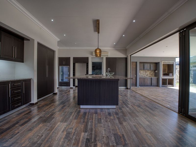 Spacious open-plan kitchen featuring dark cabinetry, granite countertops, and a central island, seamlessly flowing through stacking doors to an outdoor patio with built-in braai.