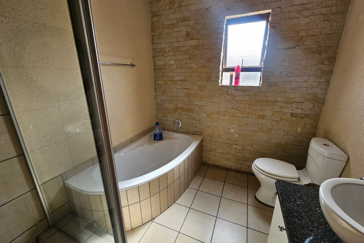 A functional bathroom featuring a built-in bathtub, glass-enclosed shower, toilet, and vanity with a stone countertop and stone-cladding feature wall.