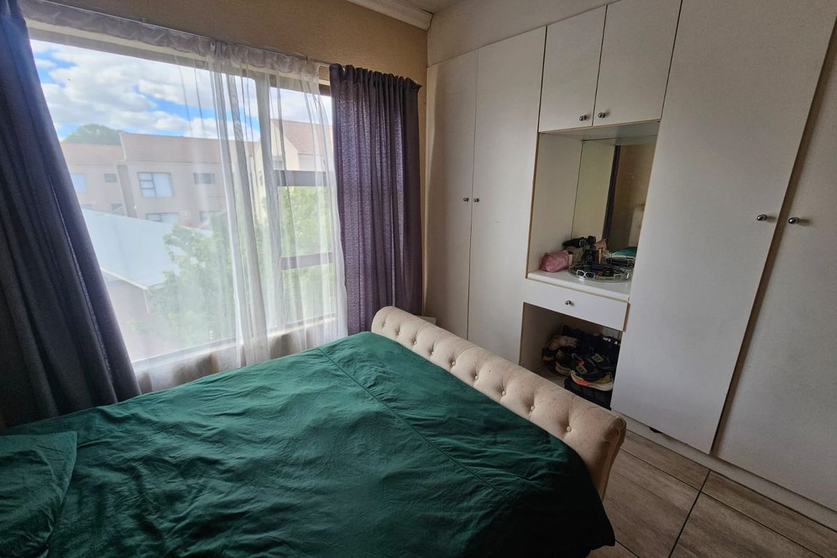 A bedroom featuring built-in floor-to-ceiling wardrobes with an integrated vanity mirror and large windows providing natural light.