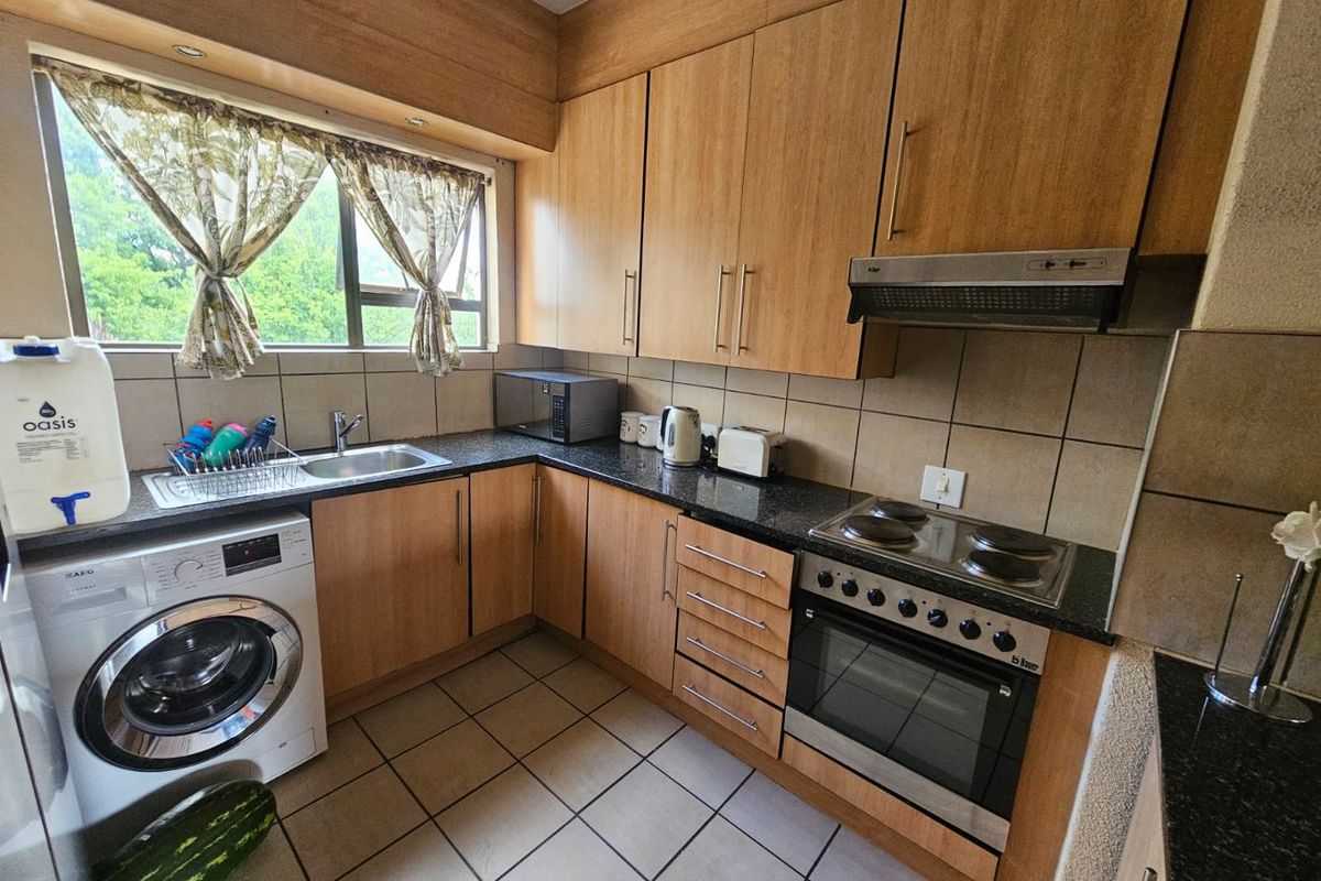 A functional kitchen featuring wood-look cabinetry, dark granite countertops, a built-in oven with hob, extractor fan, and integrated laundry plumbing.