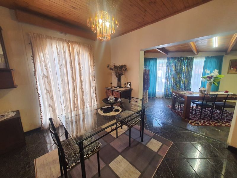 Open plan dining area featuring dark tiled flooring, timber ceilings with exposed beams, and a decorative chandelier, creating a warm and traditional atmosphere.