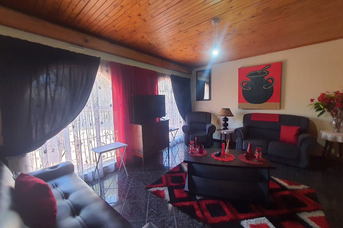A living room featuring a timber-clad ceiling, tiled flooring, and large windows with security gates, offering a functional and cozy living space.