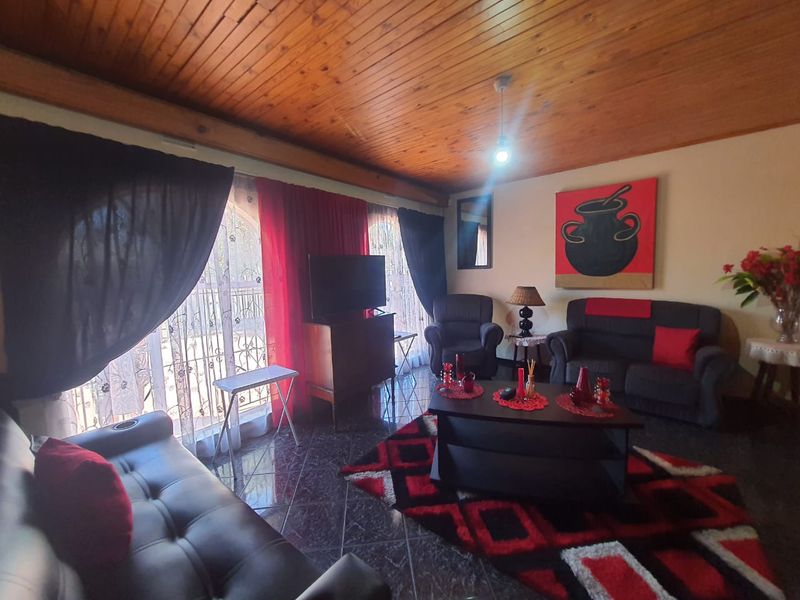 A living room featuring a timber-clad ceiling, tiled flooring, and large windows with security gates, offering a functional and cozy living space.