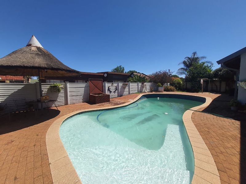 Outdoor pool area featuring a swimming pool, paved surround, and a traditional thatched lapa, providing a functional space for outdoor recreation.