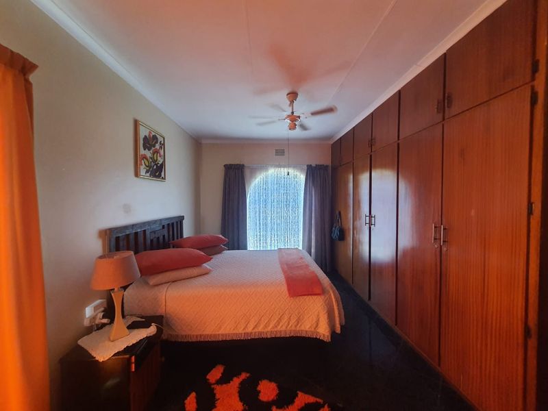 A bedroom featuring extensive floor-to-ceiling built-in wooden cupboards, a ceiling fan, and coving detail.