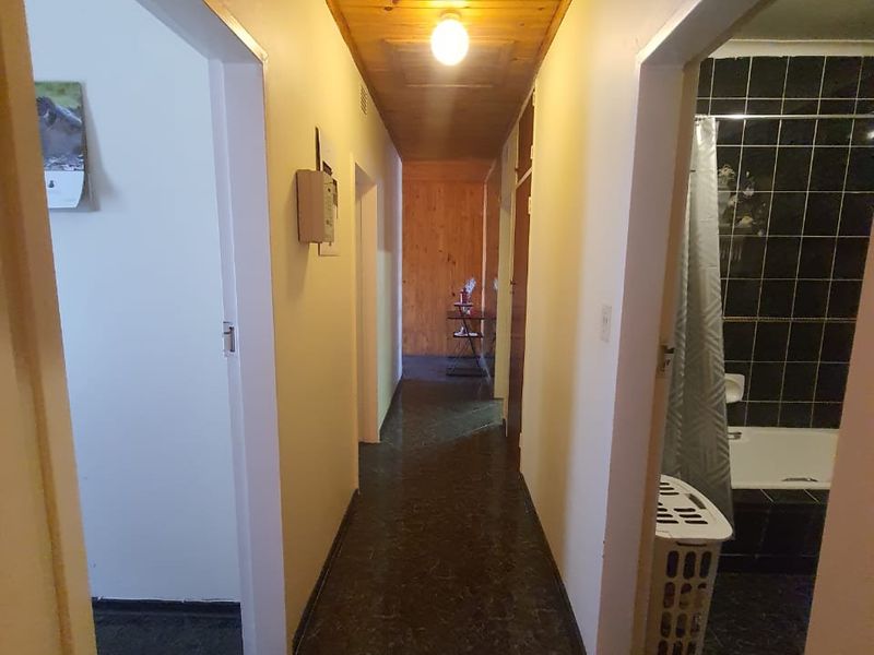 A narrow hallway featuring a timber-paneled ceiling and dark tiled flooring, providing access to adjacent rooms including a bathroom.