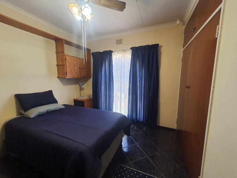 A functional bedroom featuring dark tiled flooring, built-in wooden cupboards, and wall-mounted storage shelving.