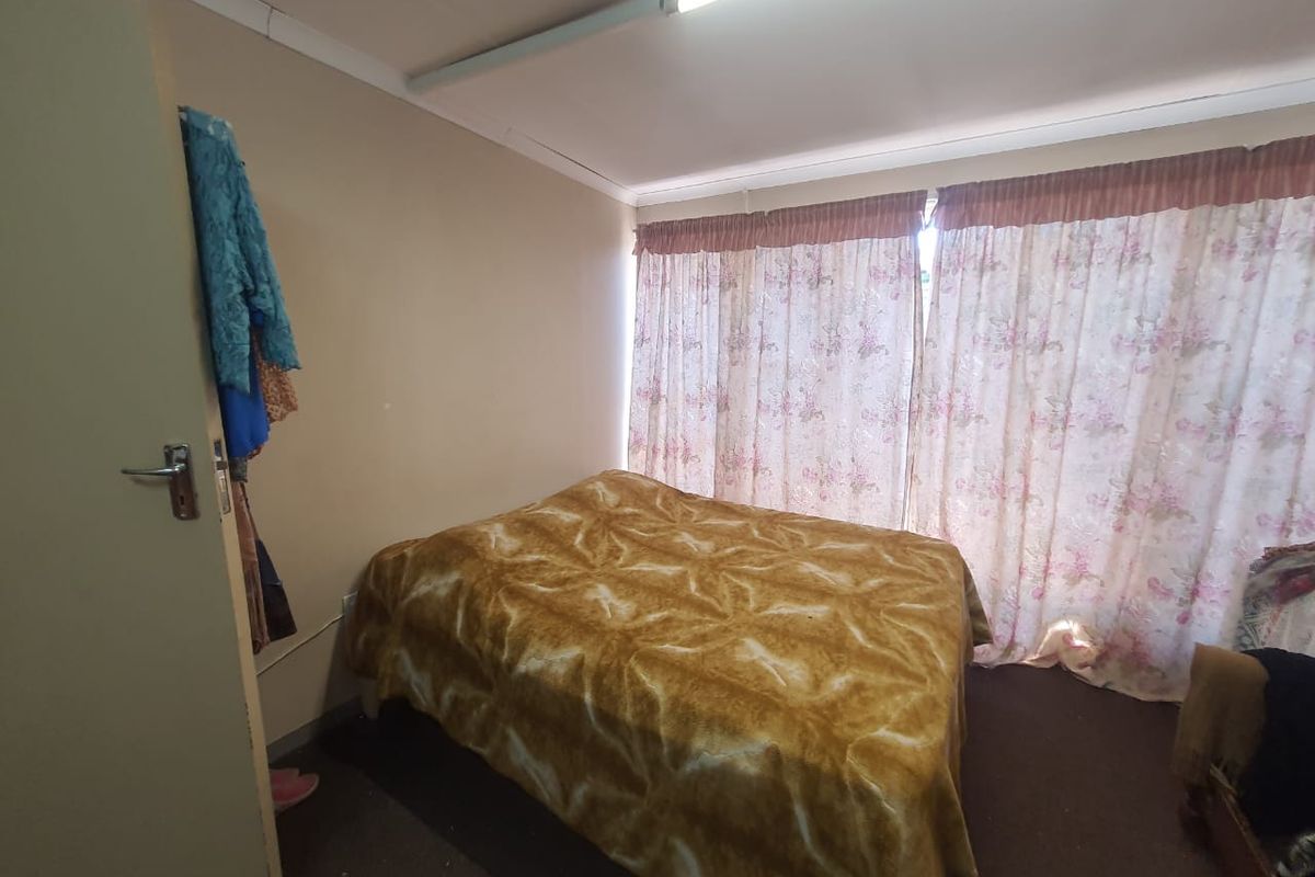 A bedroom featuring neutral wall tones, a fluorescent light fixture, and floor-to-ceiling curtains covering the window area.