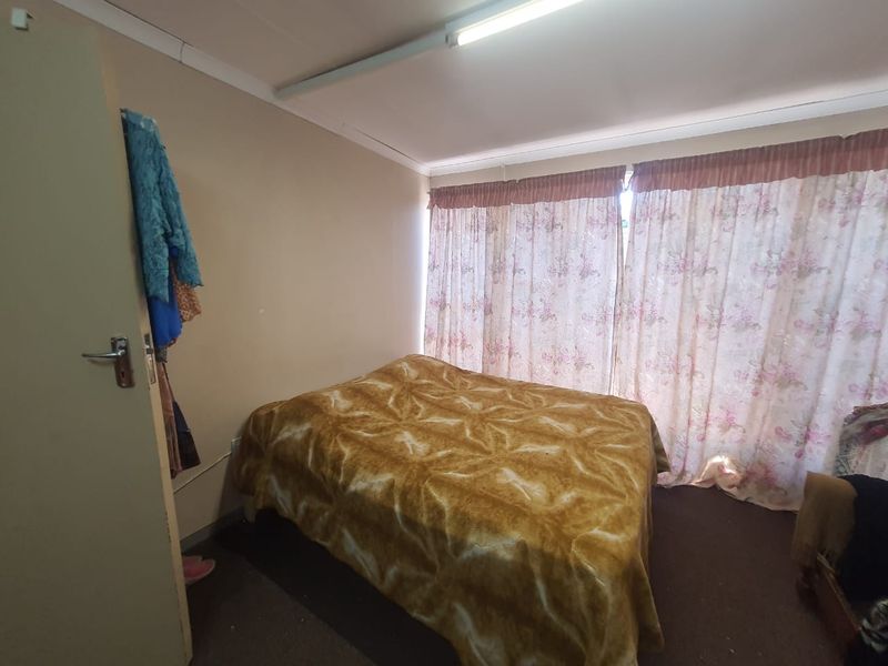 A bedroom featuring neutral wall tones, a fluorescent light fixture, and floor-to-ceiling curtains covering the window area.