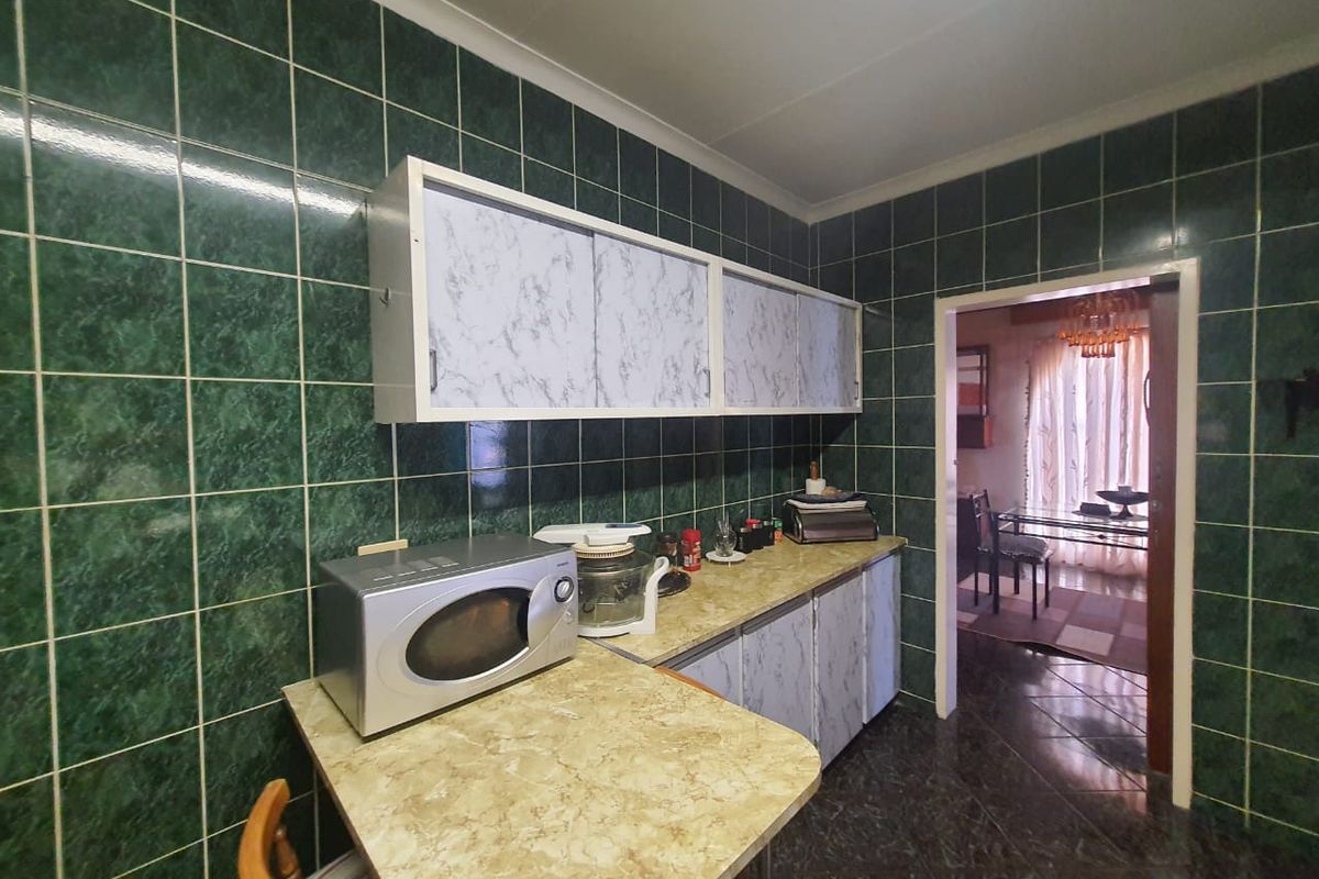 A dated kitchen featuring dark green wall tiles, laminate countertops, and built-in cabinetry, offering significant potential for a modern renovation.