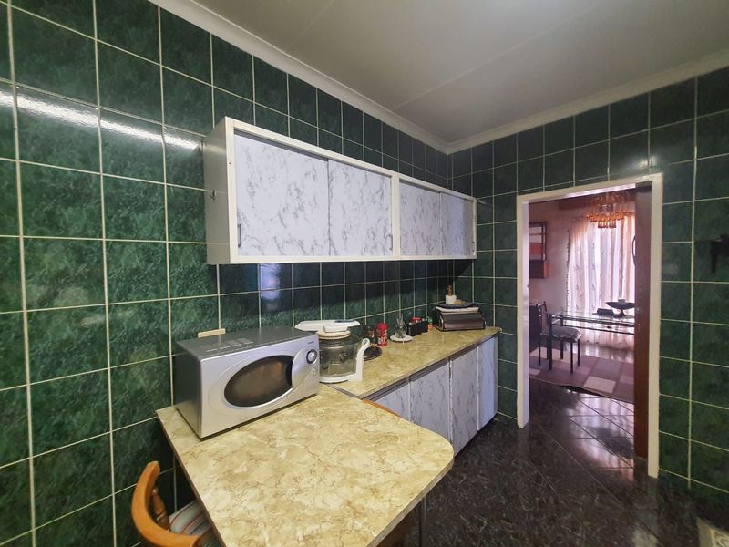 A dated kitchen featuring dark green wall tiles, laminate countertops, and built-in cabinetry, offering significant potential for a modern renovation.