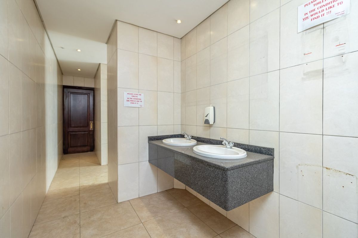 A functional office restroom featuring a dual-basin vanity with granite countertop and full-height wall tiling.