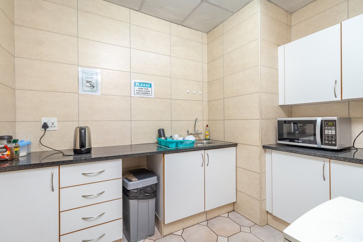 A functional office kitchenette featuring tiled walls, granite-look countertops, built-in white cabinetry, a stainless steel sink, and a built-in microwave.