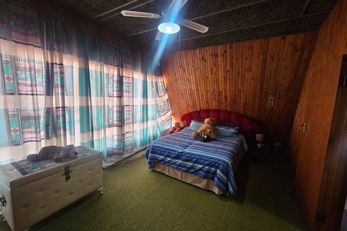 A bedroom featuring wood-paneled walls, a ceiling fan, and carpeted flooring, offering a rustic aesthetic with potential for modernization.