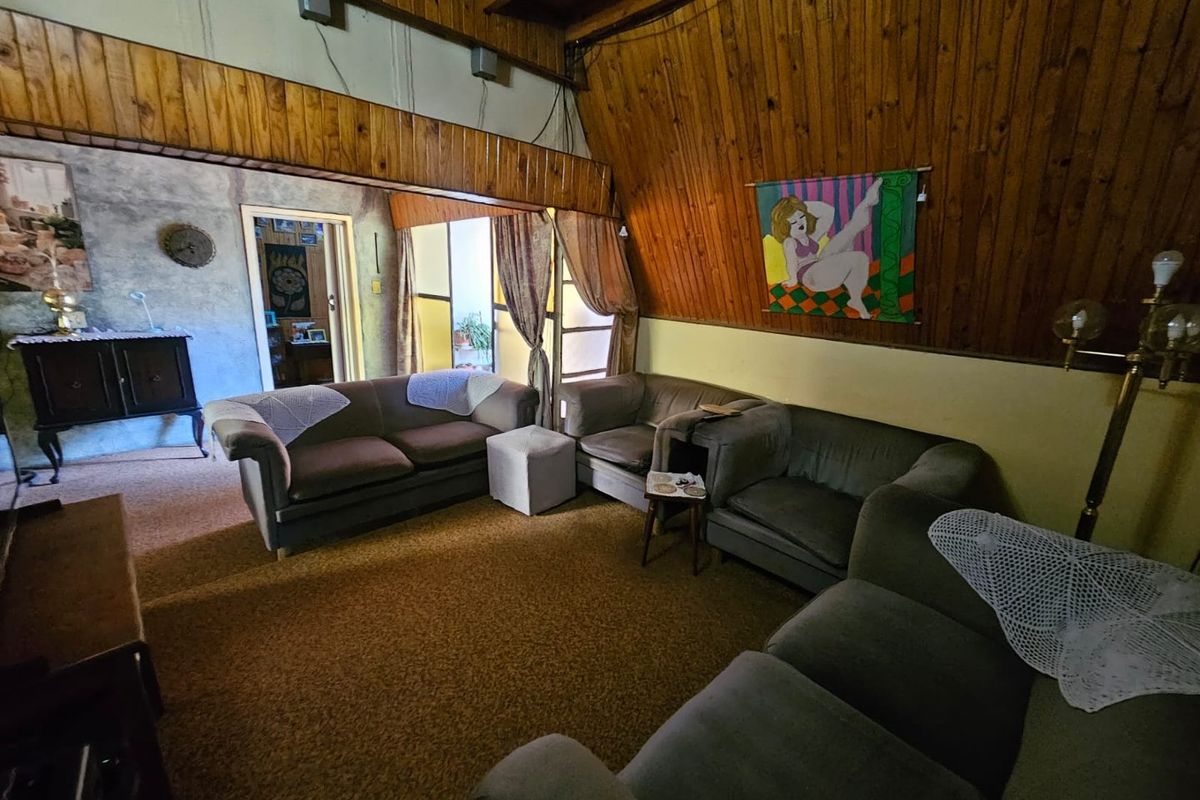 Spacious living area featuring vaulted timber-paneled ceilings, carpeted flooring, and direct access to an adjoining room.
