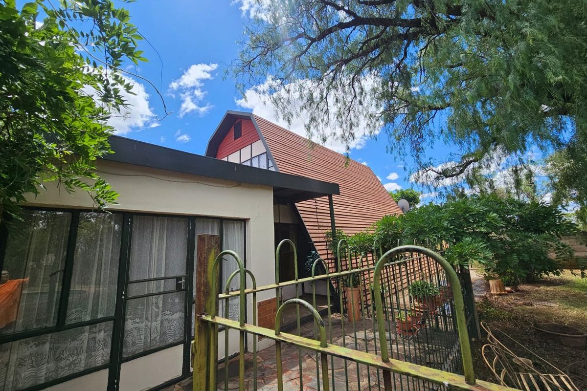 Exterior view of a farm-style property featuring a distinctive A-frame roof structure, stone paving, and mature garden surroundings.