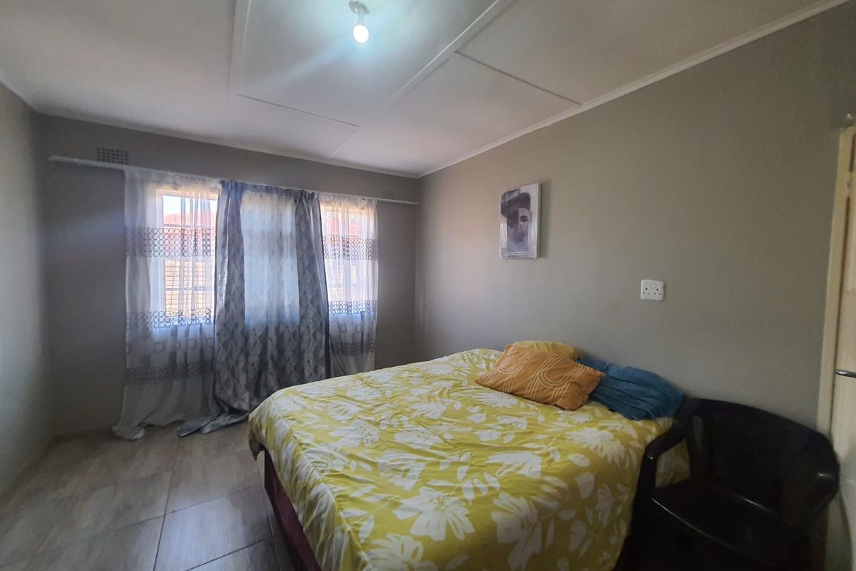 A standard bedroom featuring tiled flooring, neutral wall tones, and a window with curtain track installation.