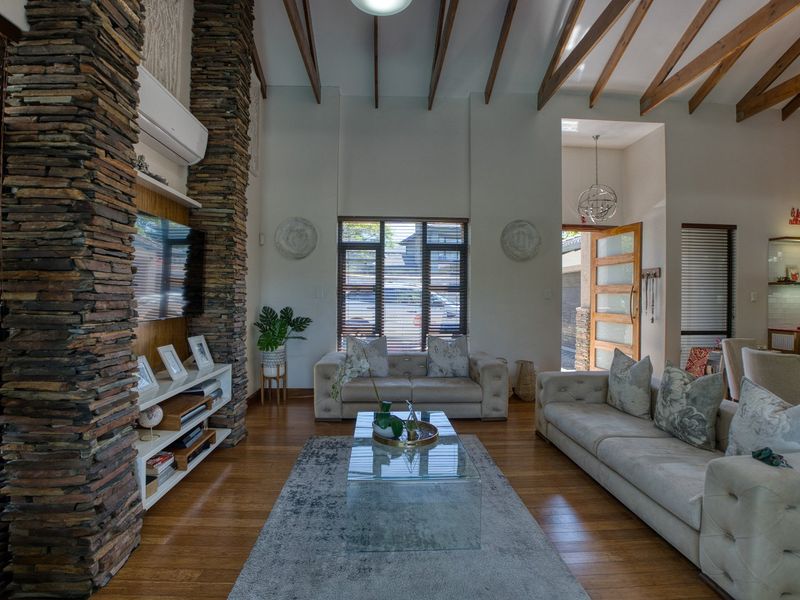 Spacious living room featuring high vaulted ceilings with exposed timber beams, hardwood flooring, and striking stacked stone feature columns.