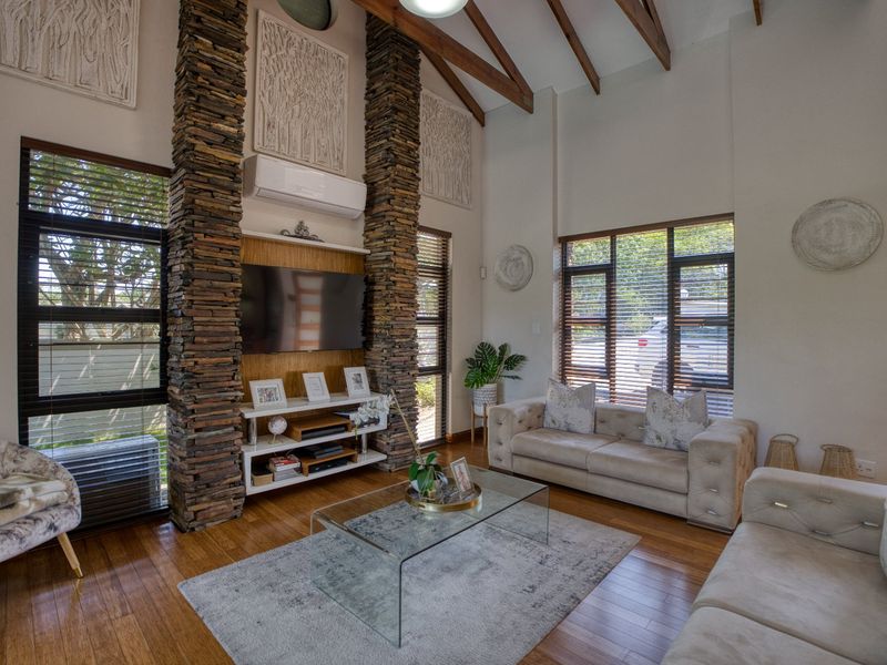 Spacious living room featuring high vaulted ceilings with exposed timber beams, striking stacked stone columns, and warm hardwood flooring.