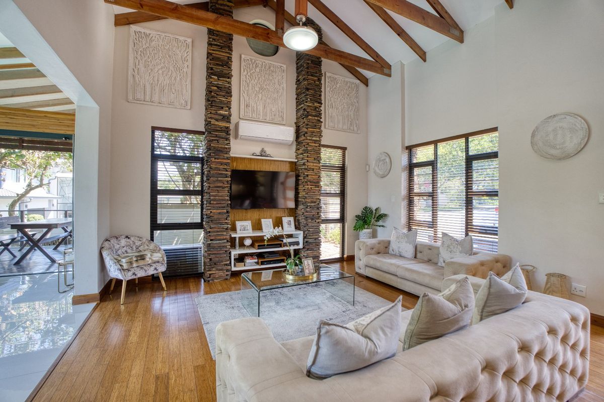 Spacious living room featuring a vaulted ceiling with exposed timber beams, a striking stacked stone fireplace feature, and large windows providing ample natural light.