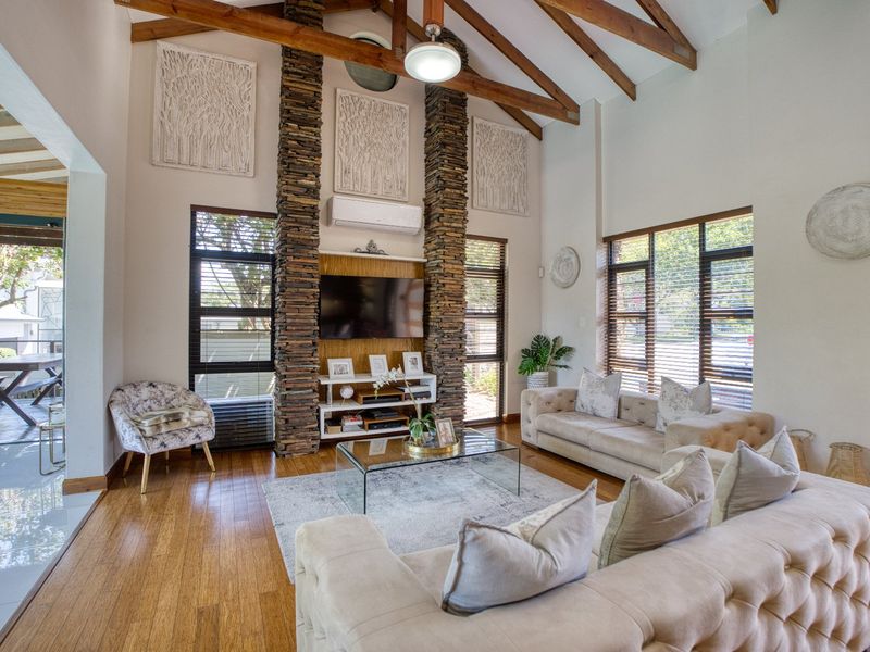 Spacious living room featuring a vaulted ceiling with exposed timber beams, a striking stacked stone fireplace feature, and large windows providing ample natural light.