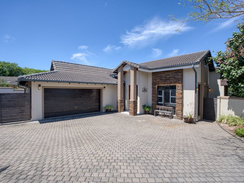 Front elevation of a well-maintained house featuring a paved driveway, double garage, and attractive stone cladding accents on the facade.