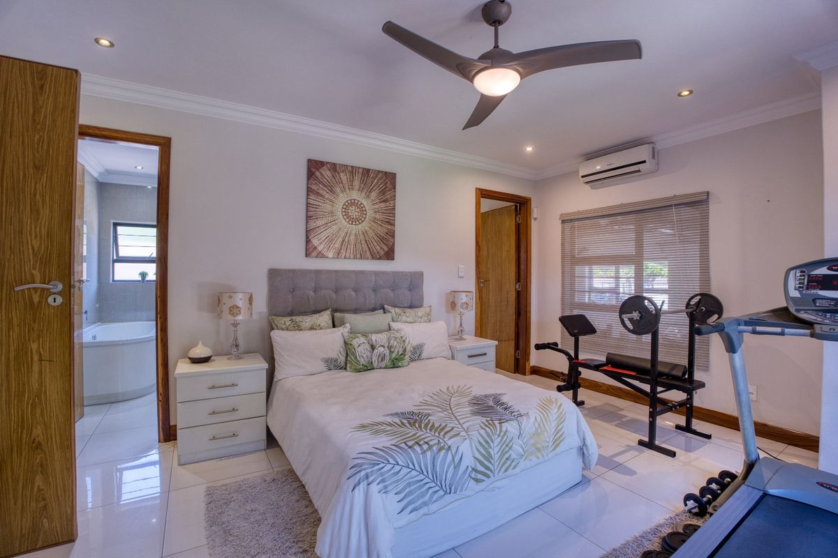 Spacious bedroom featuring tiled flooring, a ceiling fan, and a split-system air conditioner, with an adjoining en-suite bathroom visible through the doorway.