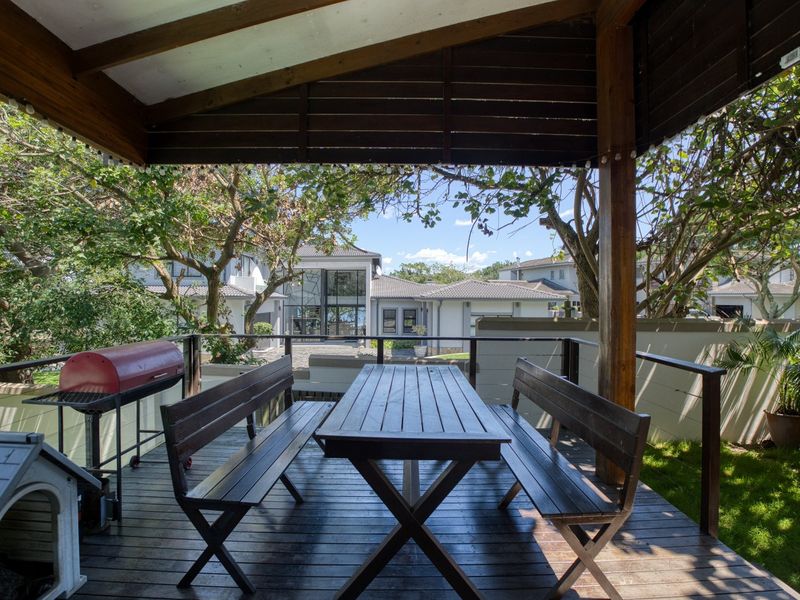 A covered timber deck patio featuring a pergola structure, overlooking a landscaped garden and the rear elevation of the property.