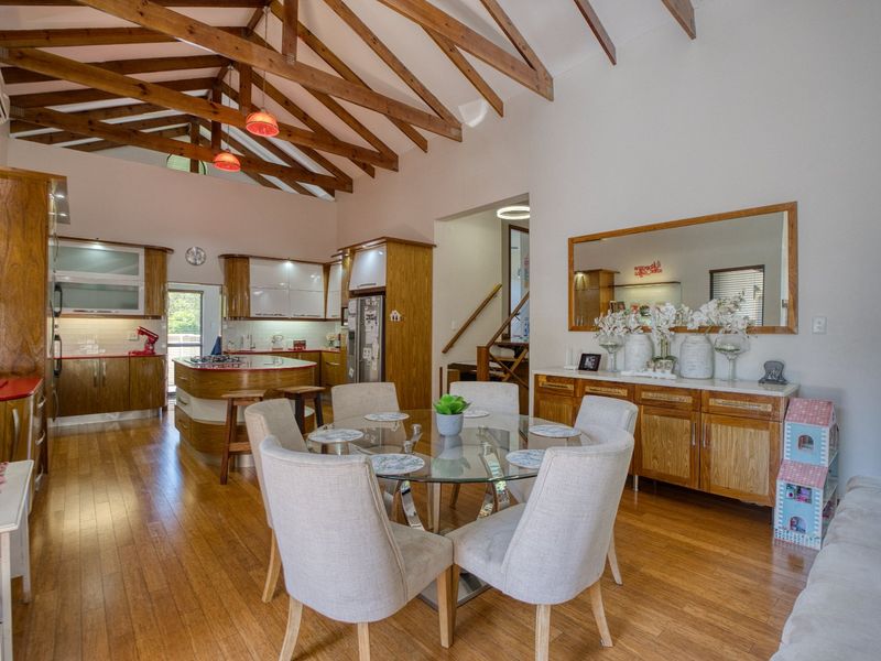 Spacious open-plan living and dining area featuring high vaulted ceilings with exposed timber rafters, hardwood flooring, and a well-appointed kitchen with island.