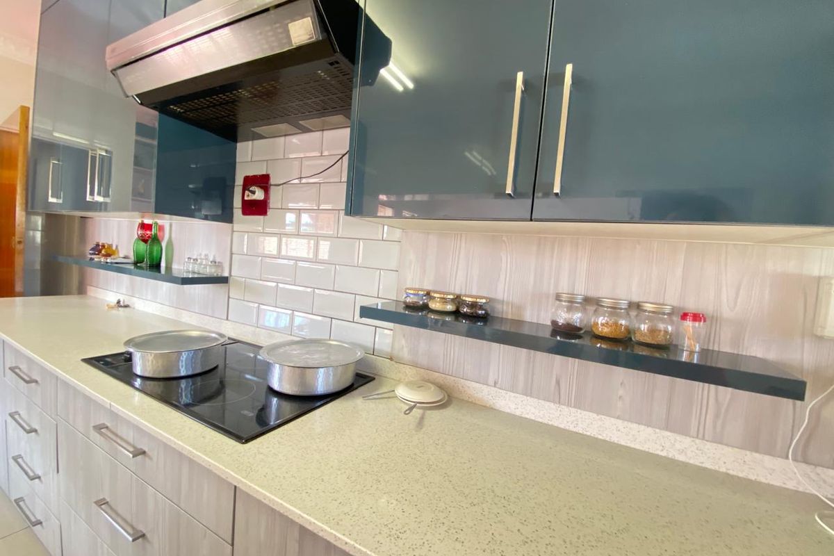 Modern kitchen featuring sleek dark cabinetry, stone countertops, subway tile backsplash, and a built-in induction hob with an overhead extractor fan.
