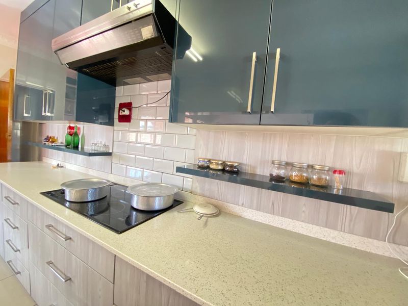 Modern kitchen featuring sleek dark cabinetry, stone countertops, subway tile backsplash, and a built-in induction hob with an overhead extractor fan.