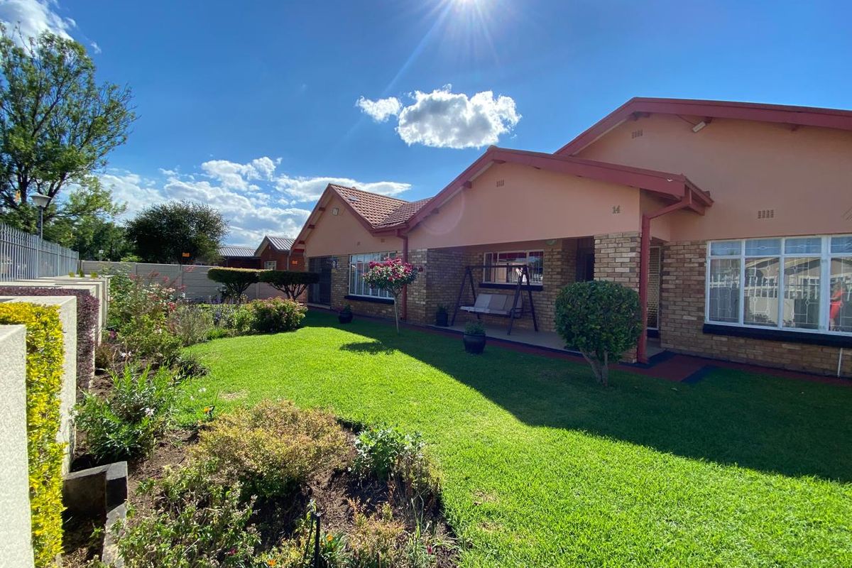 A well-maintained rear exterior view featuring a brick facade, tiled roof, covered patio area, and a neatly landscaped garden.
