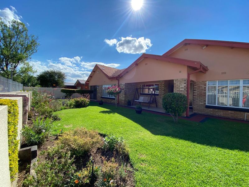 A well-maintained rear exterior view featuring a brick facade, tiled roof, covered patio area, and a neatly landscaped garden.