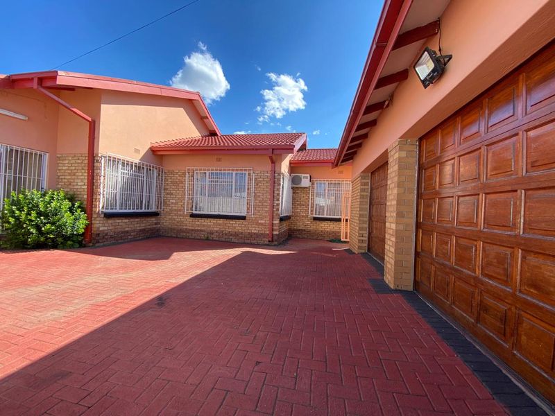 A well-maintained front exterior view featuring brick paving, wooden garage doors, and secure window bars under a tiled roof.