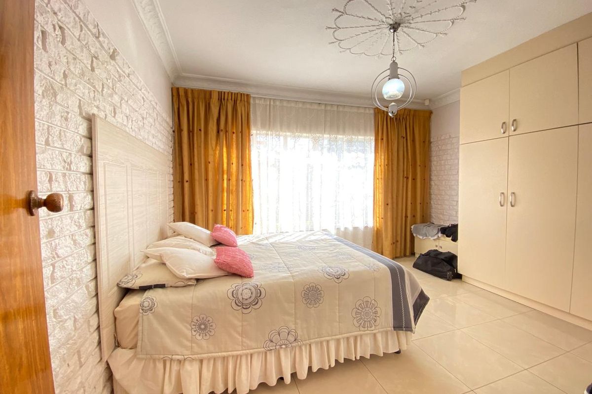 Spacious bedroom featuring a textured brick feature wall, built-in floor-to-ceiling cupboards, decorative ceiling rose, and neutral tiled flooring.