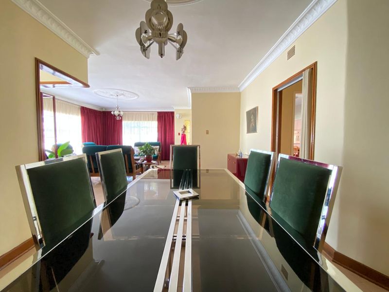 A formal dining area featuring ornate crown molding, decorative ceiling roses, and hardwood flooring, flowing into an adjacent living space.