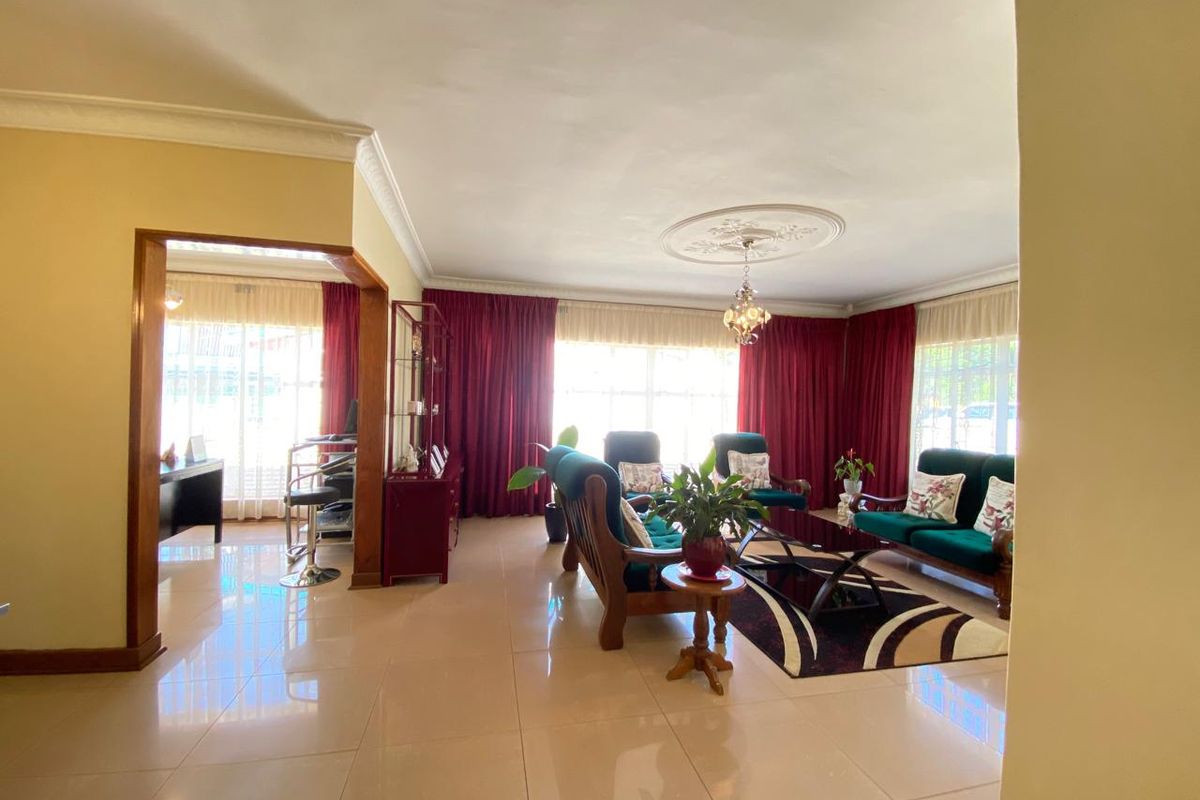 Spacious living room featuring polished tile flooring, decorative ceiling rose with chandelier, and coving, offering a bright and open living environment.