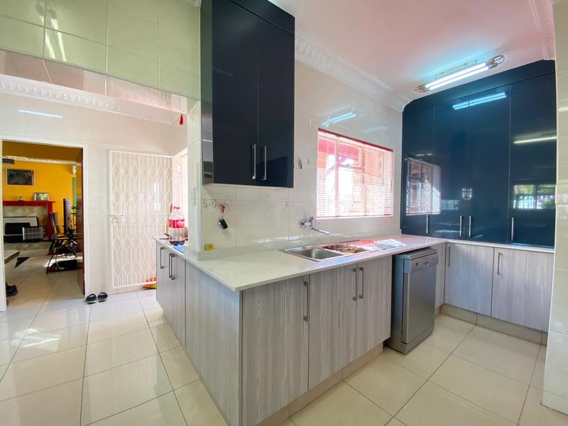 A functional kitchen featuring modern two-tone cabinetry, stone countertops, stainless steel sink, and tiled finishes throughout, with an adjacent access point.