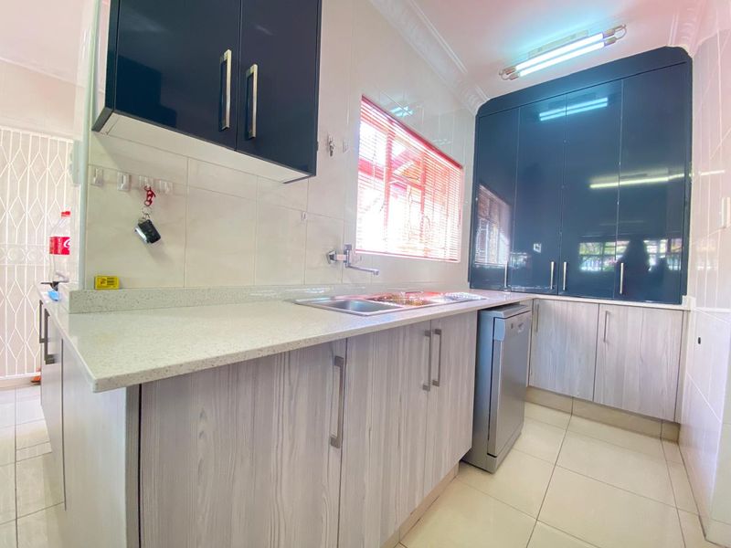 A functional kitchen featuring modern two-tone cabinetry, stone countertops, a stainless steel sink, and tiled finishes throughout.