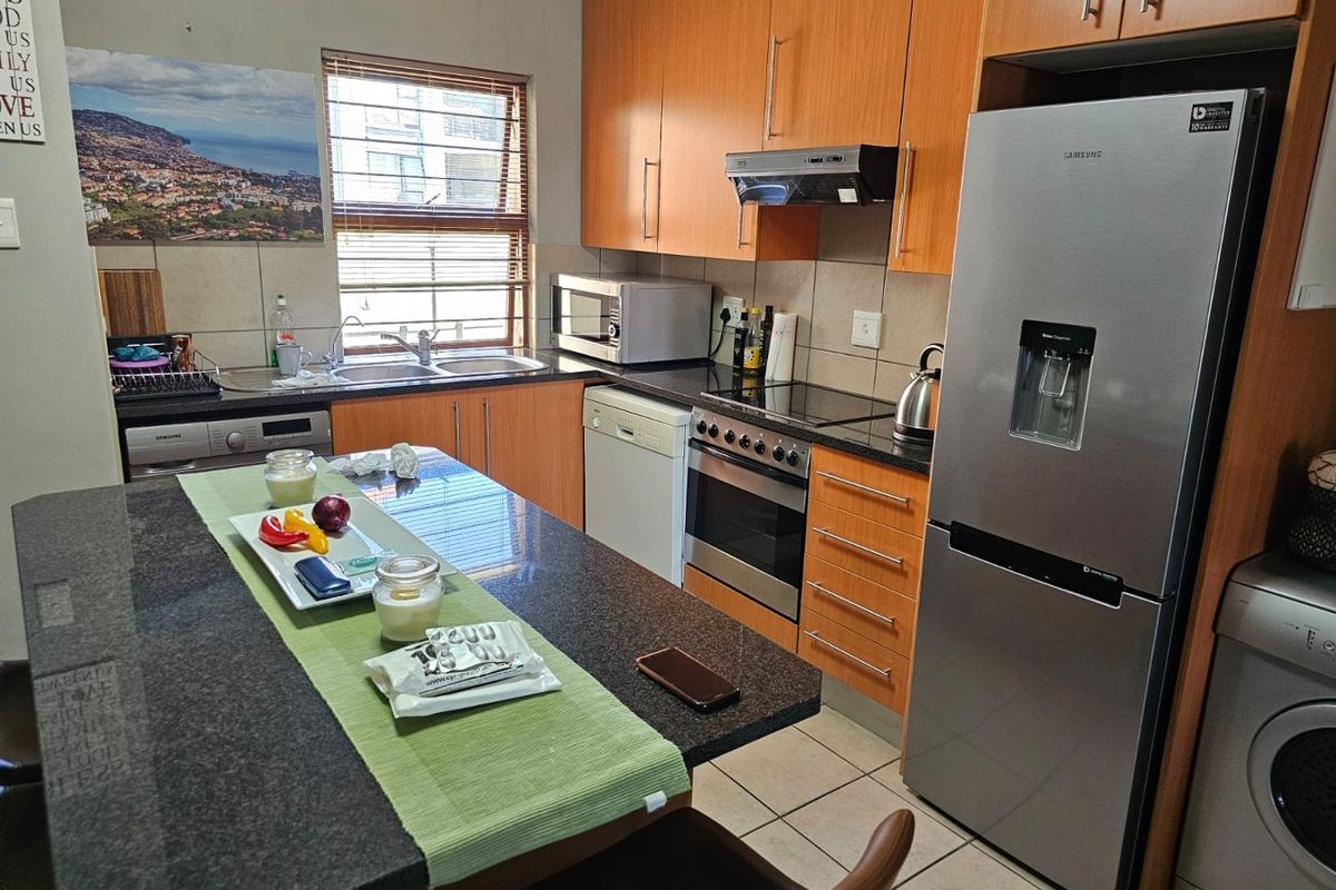A functional kitchen featuring wood-finish cabinetry, granite countertops, a built-in oven with hob, extractor fan, and integrated space for appliances.