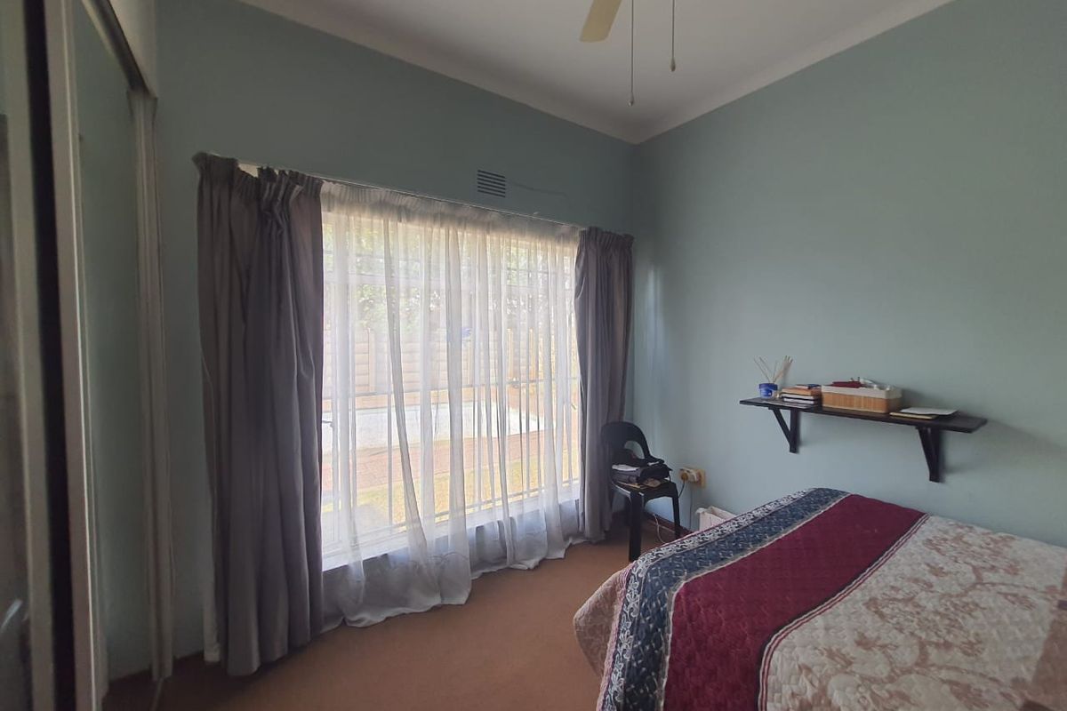 A bedroom featuring built-in sliding door cupboards, a ceiling fan, and a large window overlooking the garden area.