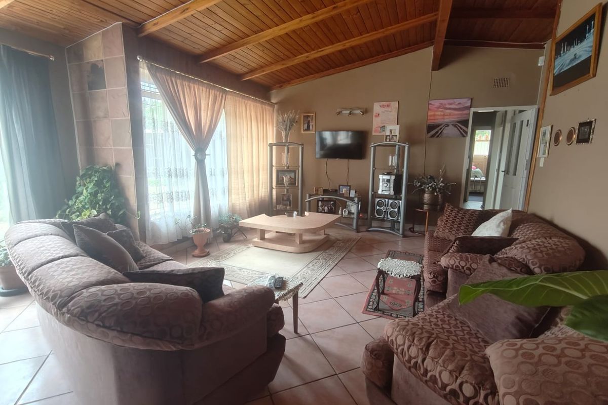 Spacious living room featuring a high vaulted timber-clad ceiling, tiled flooring, and large windows allowing for ample natural light.