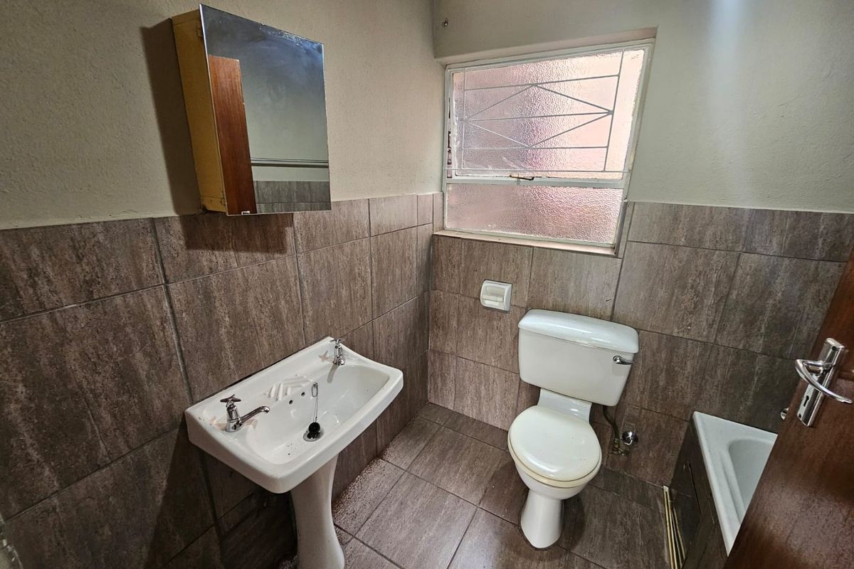 A functional bathroom featuring a pedestal basin, toilet, and tiled walls, offering a practical layout with natural light from a window.