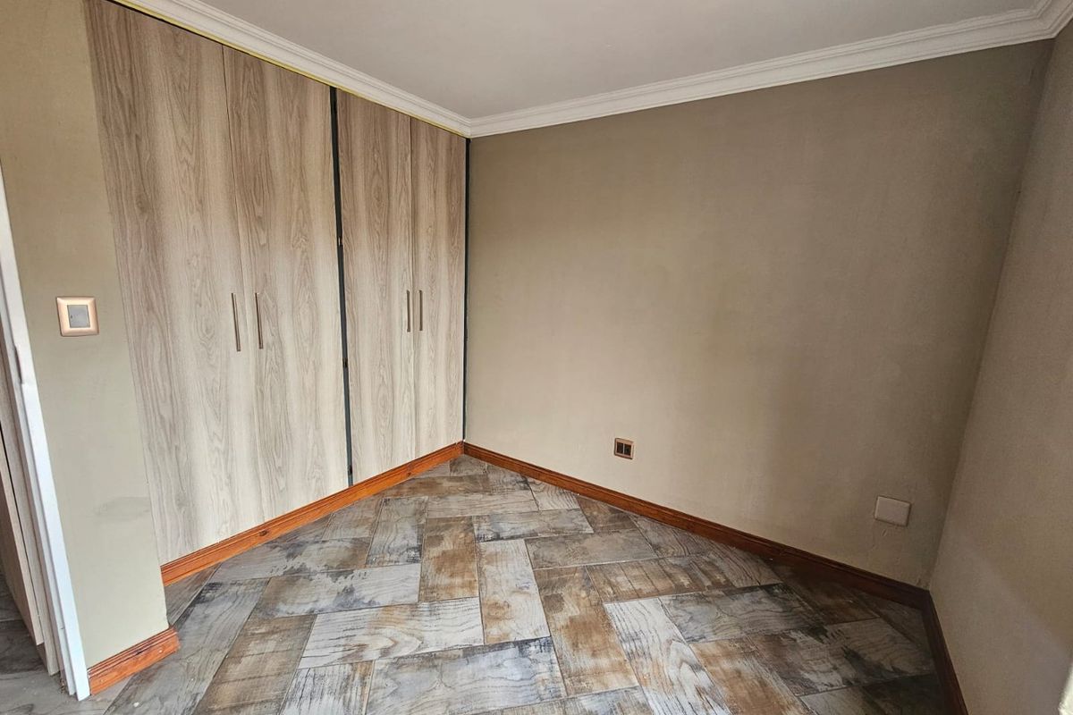 A clean, empty bedroom featuring wood-look tile flooring and built-in floor-to-ceiling wardrobes with a light wood finish.